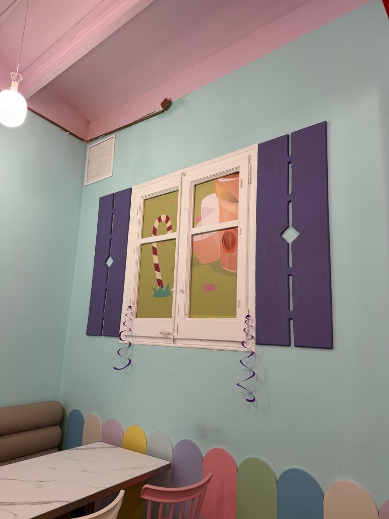 Decorative window with lilac shutters and a candy mural inside Charlie